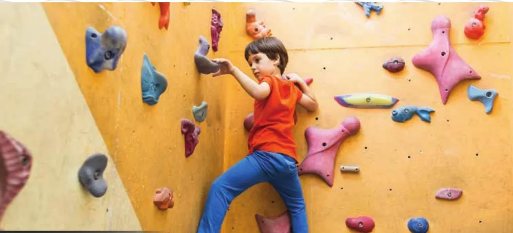 Child on a rock climbing wall, representational image